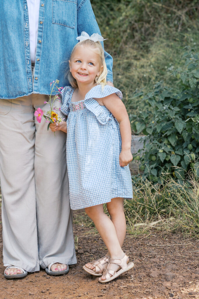 young girl smiles up at mom while standing near grandma on a trail at Golden Gate Park