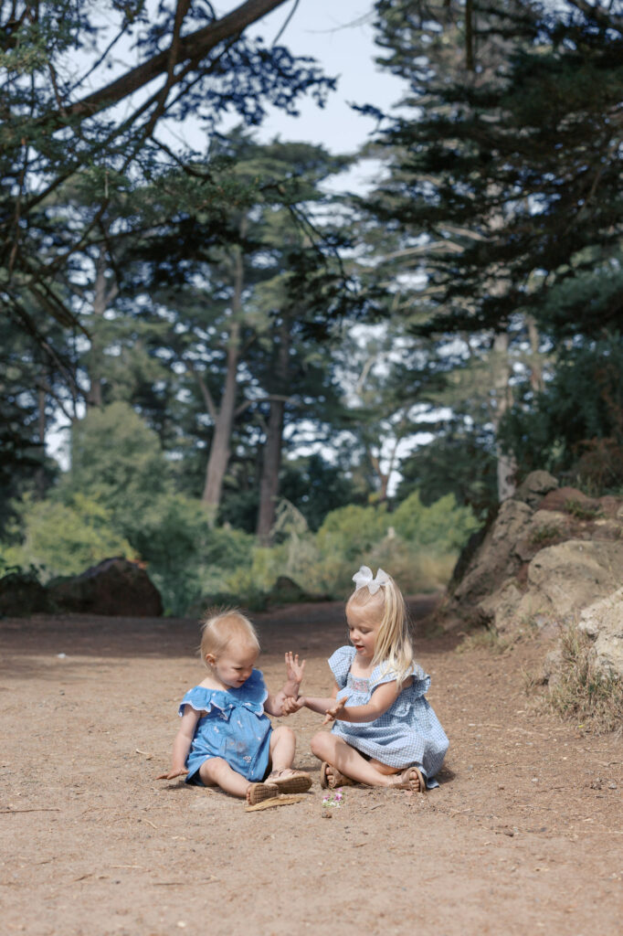 two young girls play in the dirt on a trail in Golden Gate Park during a family photography session