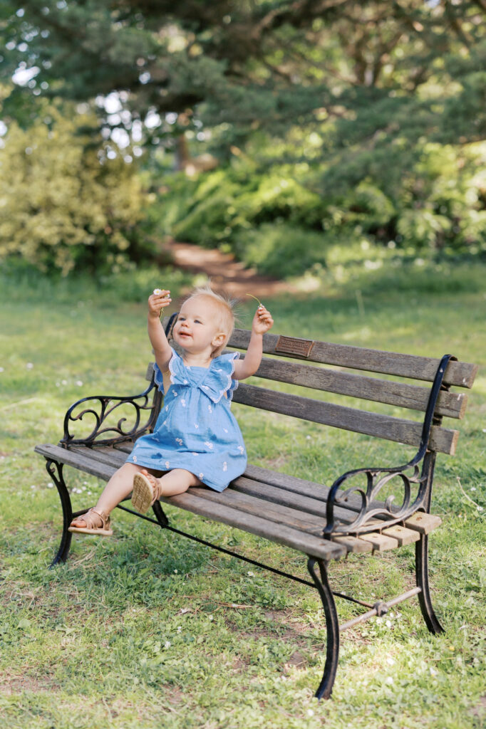 Toddler girl plays on a bench in Golden Gate park with a flower she found while exploring during her family photography session