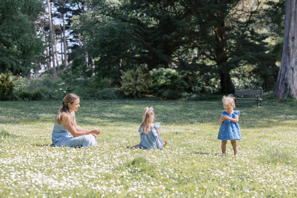 Mom sits in grass at Golden Gate Park with two young girls, picking flowers
