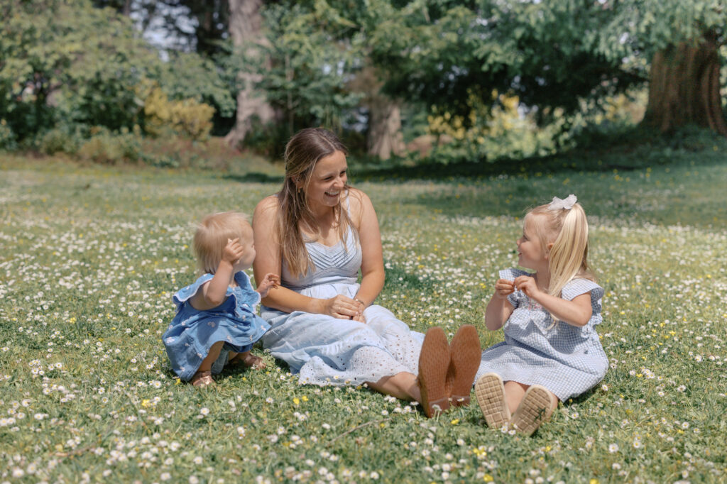 Mom sits in Golden Gate Park on the grass picking flowers with two young children during San Francisco family photography session