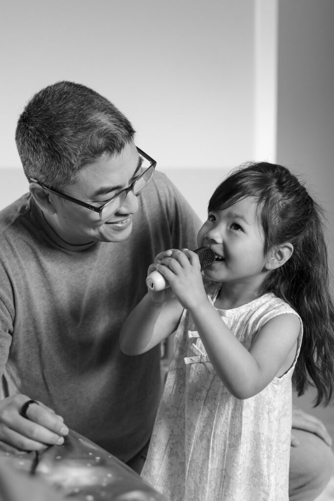 Father and toddler daughter play and sing into a microphone during a San Mateo photography session in home