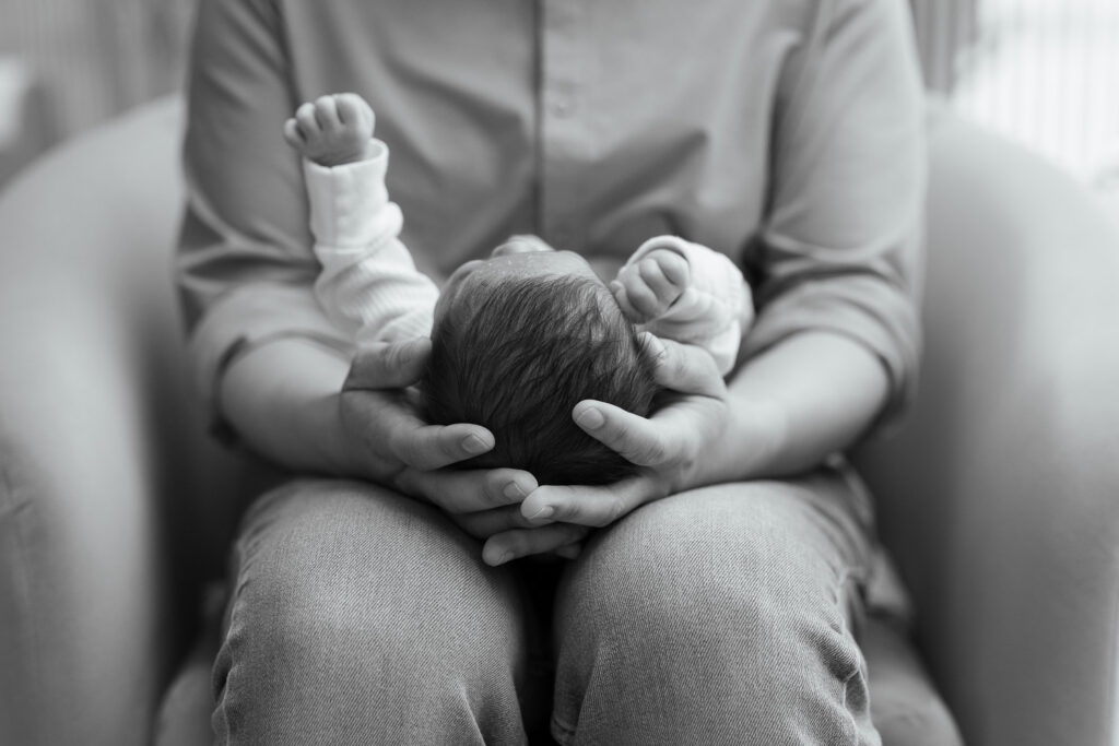 detail shot of dad holding newborn baby - focus on dads hands holding tiny newborn baby head, black and white image