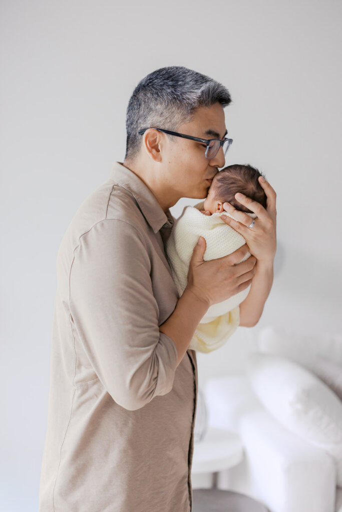 dad kisses newborn baby boys forehead in his home in San Mateo