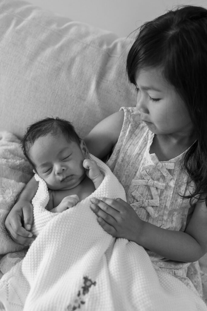 older sister gazes down at one month old baby brother during San Mateo newborn session, black and white image