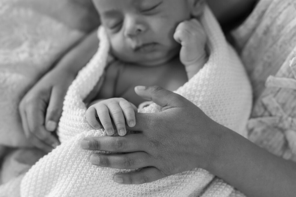 big sister holds onto newborn baby brothers fingers. Detail shot, black and white image