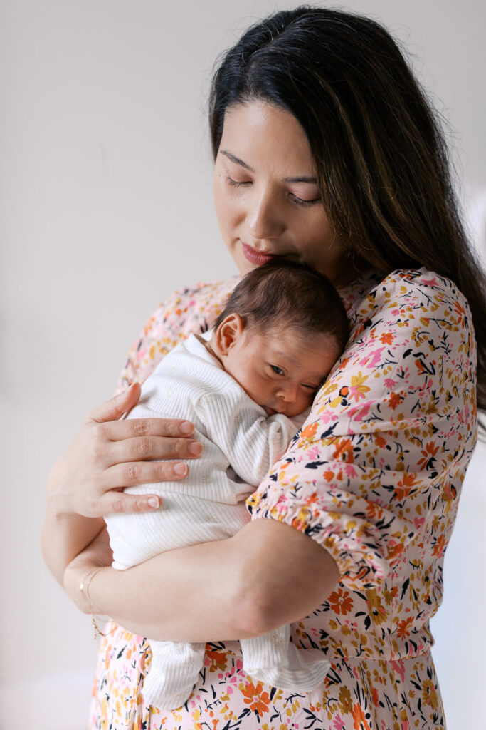 mom cuddles newborn baby boy into her chest while wearing a light floral dress