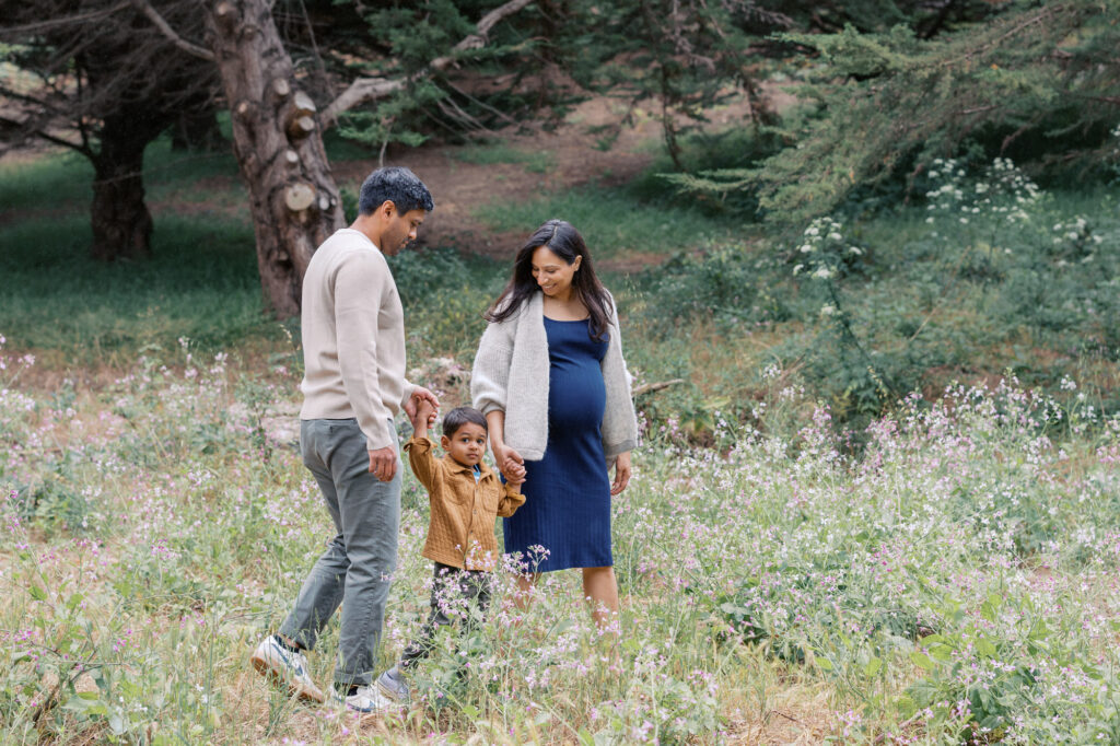 family of three walk in the wild flowers in the Presidio, San Francisco during their maternity photography session