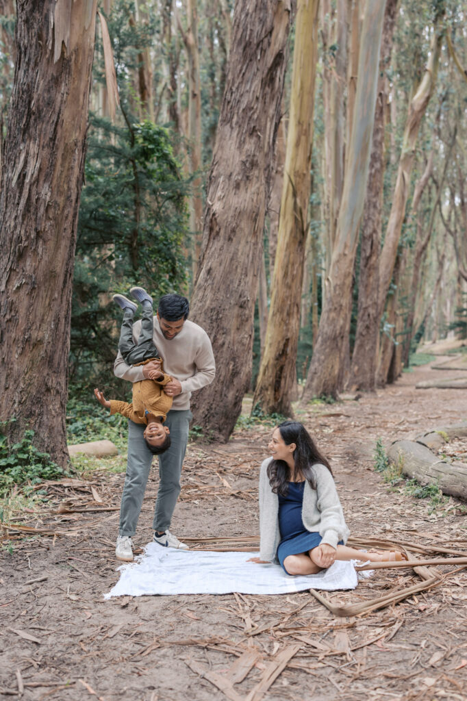 dad holds toddler upside down while mom gazes on from her seat on the blanket in Woodline, Presidio