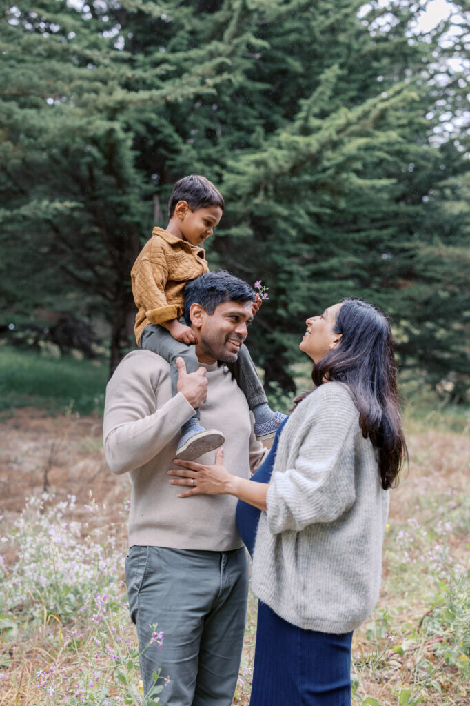 Family of three laughing in a filed of wildflowers in the Presidio, San Francisco during a family maternity photography session