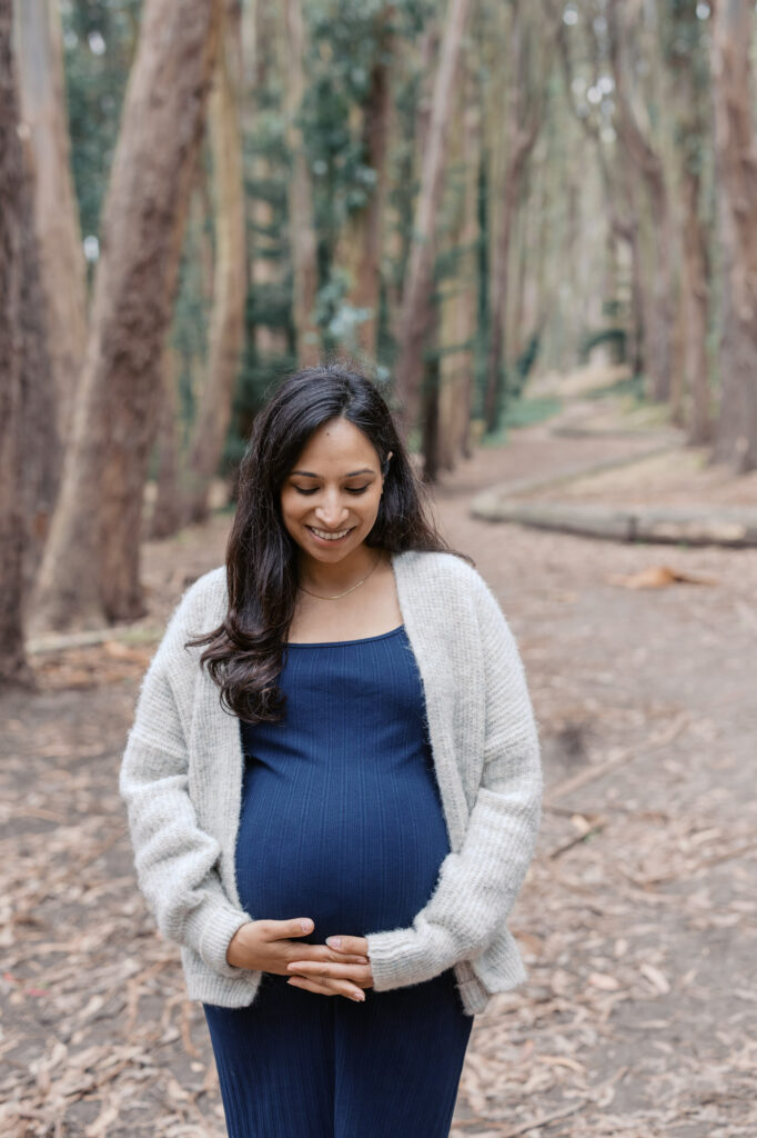 expecting mother holds her pregnant belly while standing in the trees at Woodline, Presidio during her San Francisco maternity photography session