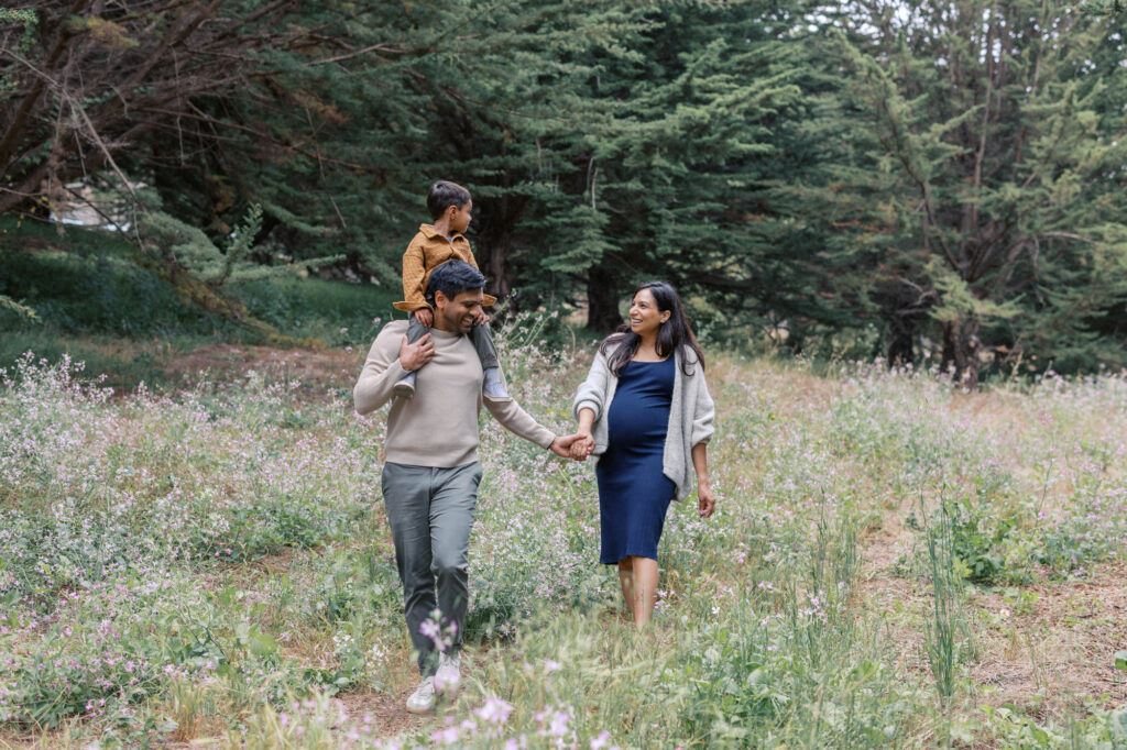 family of three walks amongst the wildflowers in the Presidio, San Francisco during maternity photography session