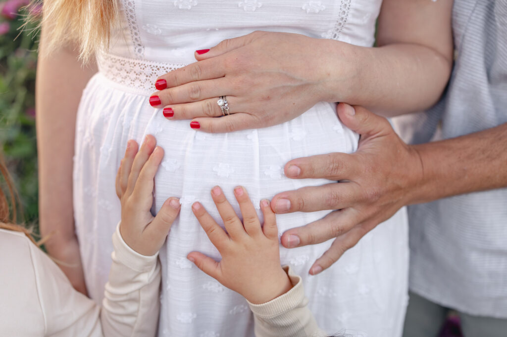 Little sisters place their hands on mama's baby belly during East Bay maternity photography session