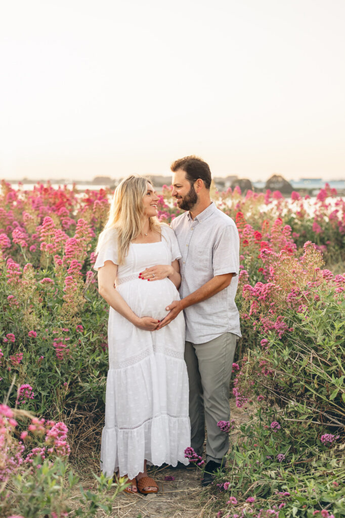Expecting couple stand in a flower field filled with pink flowers during an East Bay maternity session