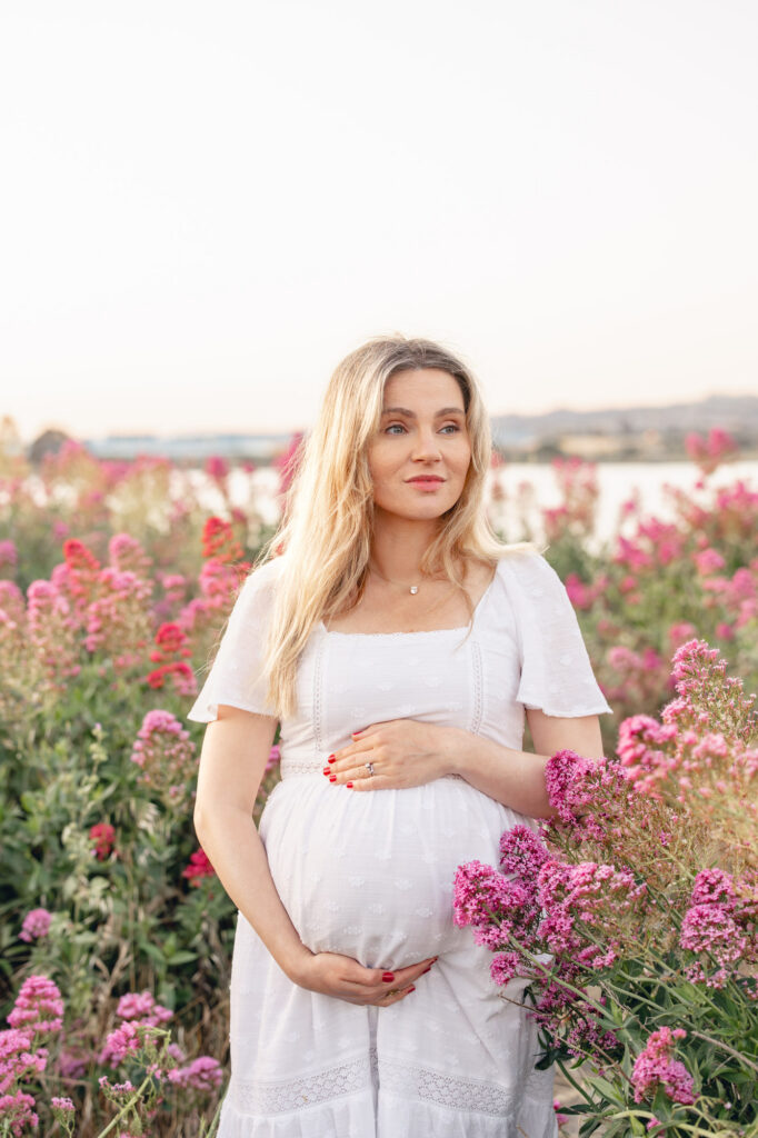 Expecting mother in white dress gazes over the pink flowers during an East Bay maternity session