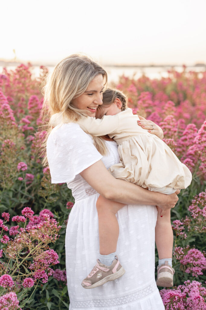 mom holds and snuggles young toddler during East Bay maternity session in pink flowers