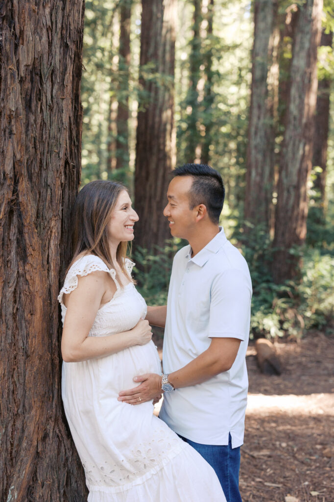 expecting mom leans against a redwood tree during her Oakland maternity session on a sunny day