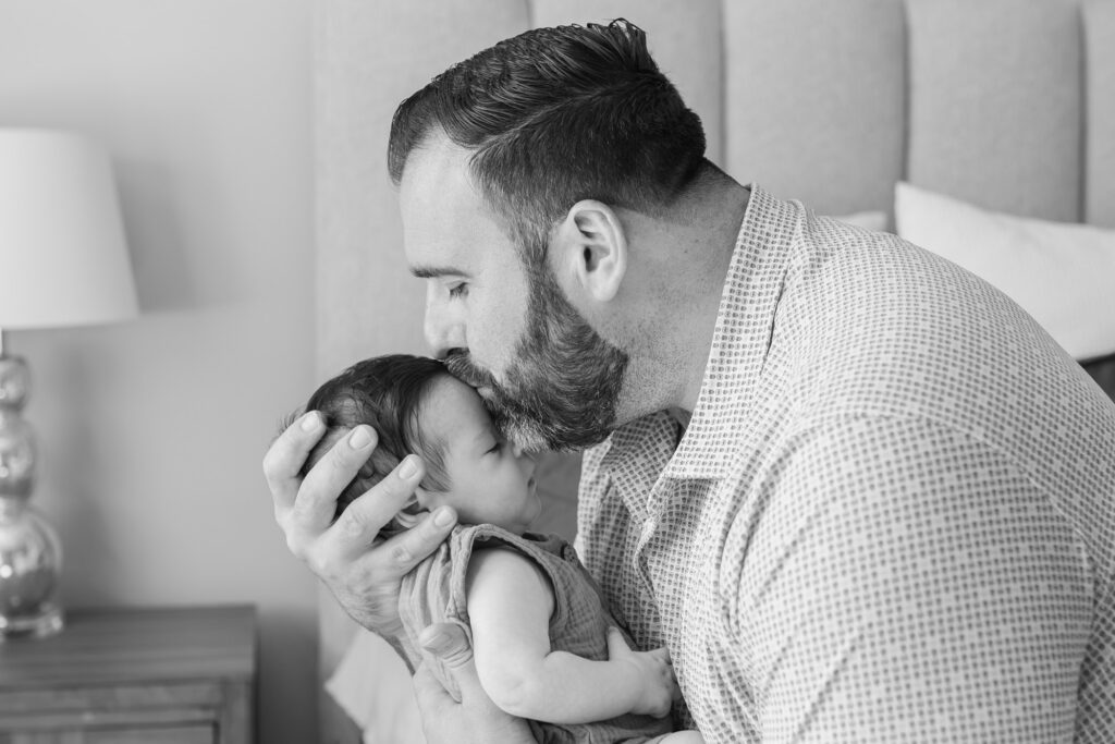new dad kisses 2 month old's forehead during newborn photography session, black and white image