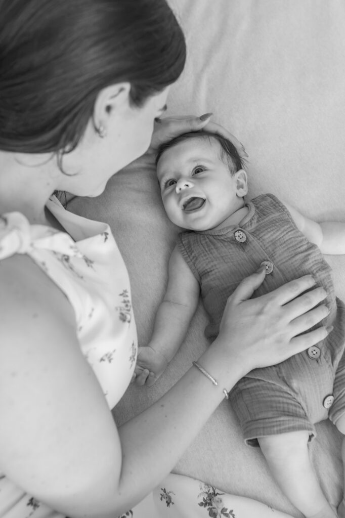 2 month old lays on bed and looks up at mom and laughs during in home newborn session