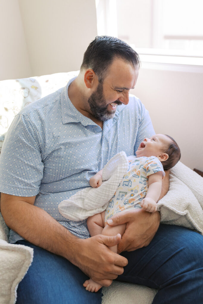 2 month old baby boy laughs at new dad's faces while they rock in the nursery rocking chair during Redwood City newborn session