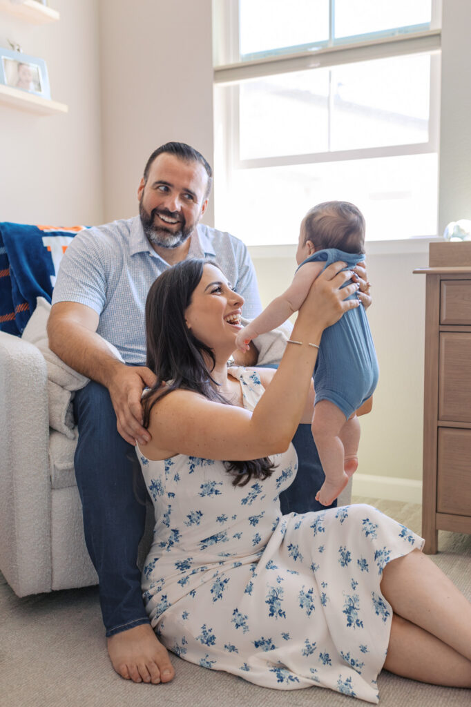 playful moment between new family of three as mom lifts 2 month old into the air in his football themed nursery in Redwood City
