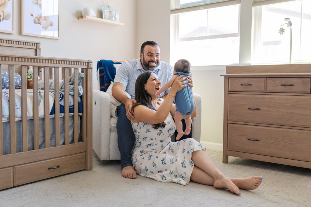 new parents lift newborn into the air in football themed nursery during 2 month old newborn session in Redwood City