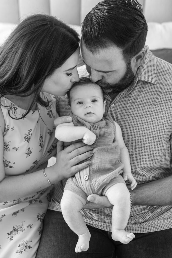new parents kiss the top of 2 month old baby's head during newborn photography session in Redwood City