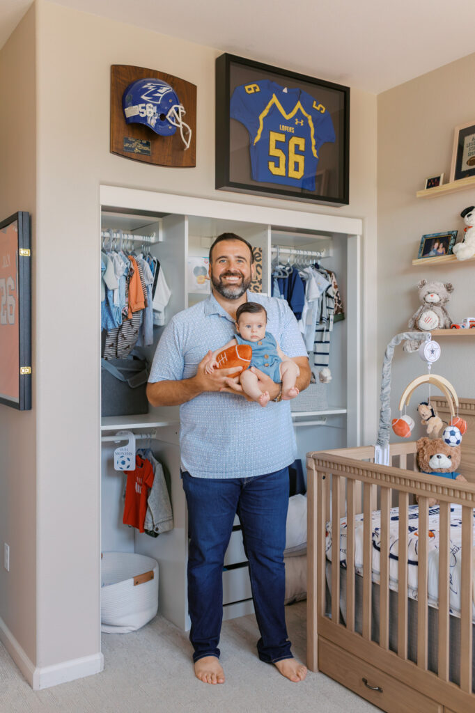 Dad stands under football memorabilia while holding the newest teammate, aka his newborn