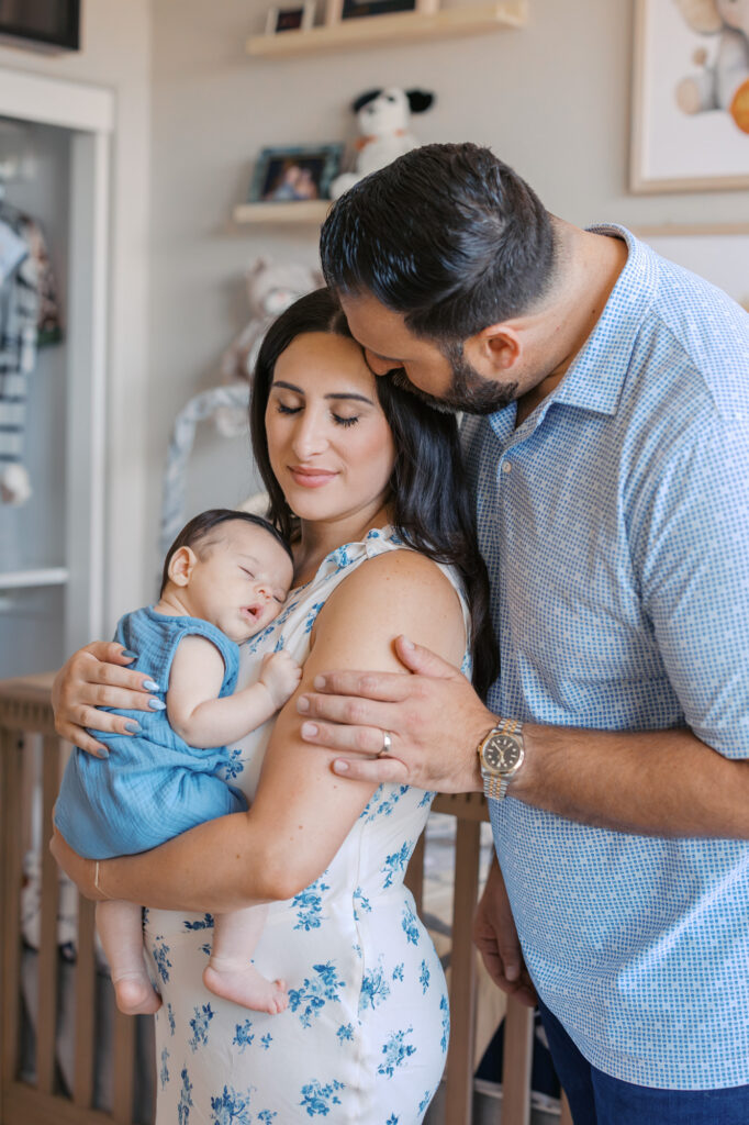 dad leans over to kiss new moms forehead while 2 month old baby boy sleeps on her chest during Redwood City newborn session