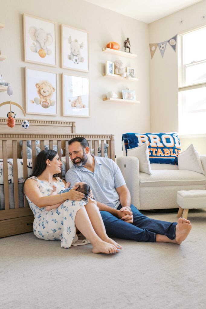new parents sit in football themed nursery with their 2 month old baby boy during Redwood City newborn session