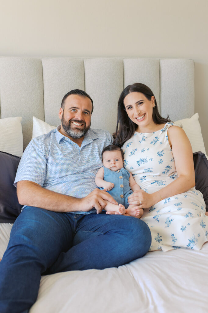 parents hold 2 month old newborn on their bed and smile for family photo during newborn photography session in Redwood City
