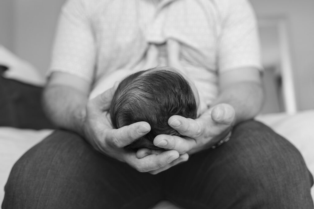 dad holds sleeping newborn, detail shot of his hands holding newborn's head for size comparison, black and white image