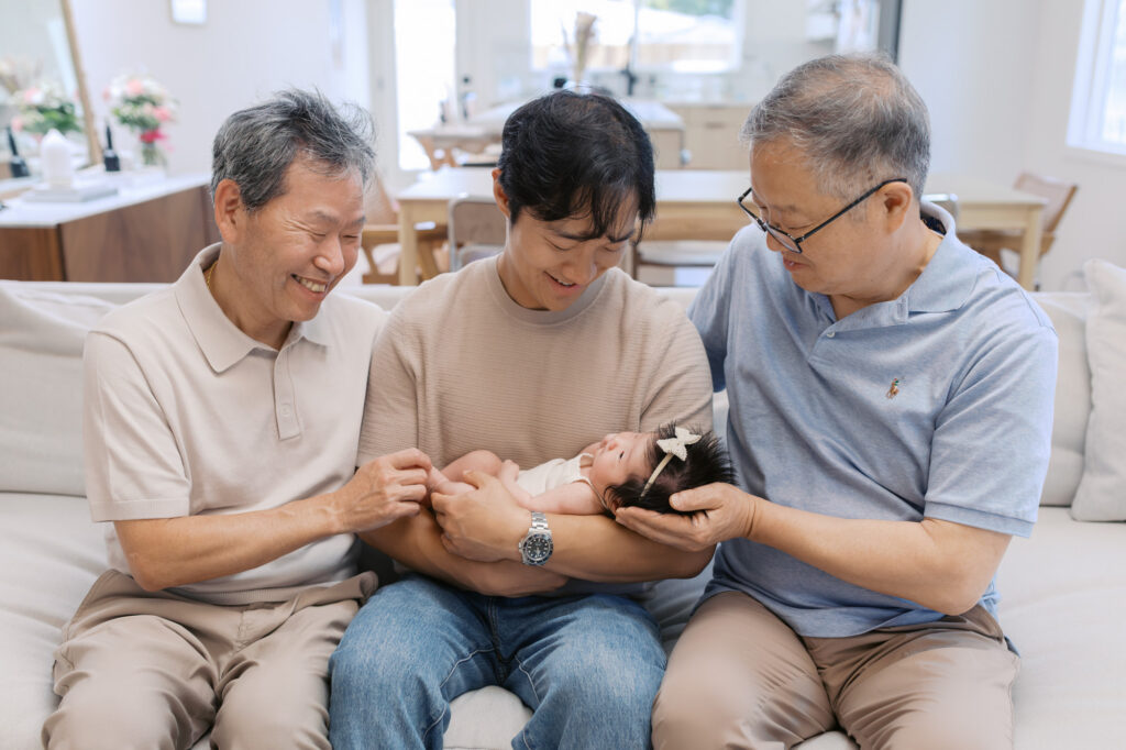 new dad and both grandfathers hold and gaze at newborn baby girl during Santa Clara in home photography session