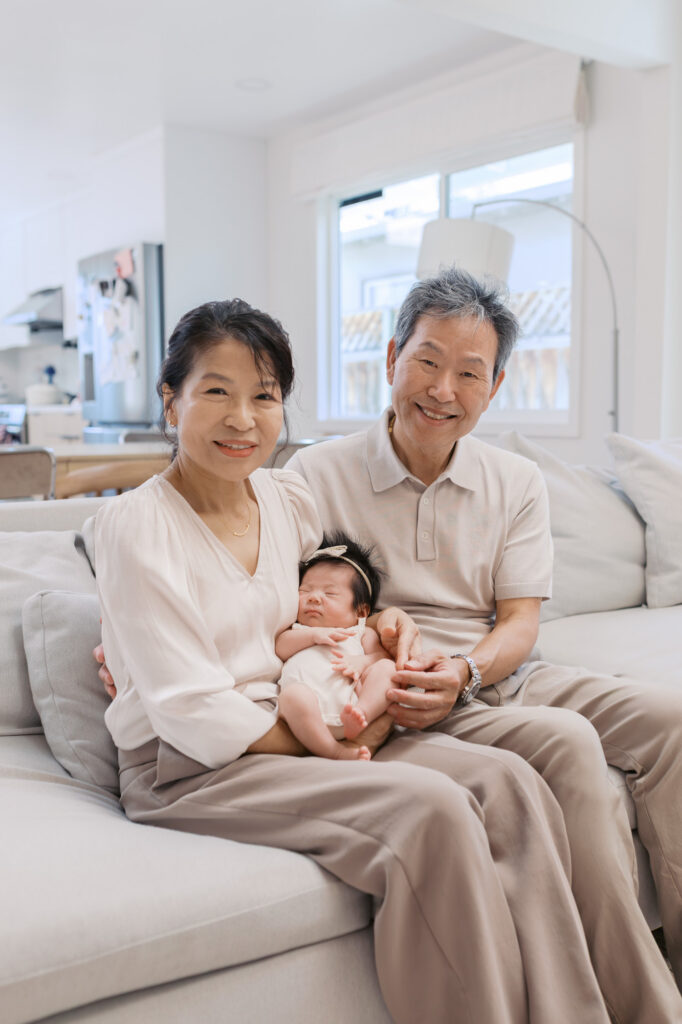 grandparents holding newborn baby girl sitting on beige couch