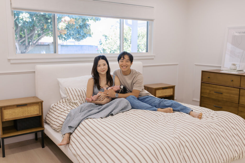 a couple sits on their bed holding their newborn baby girl during their Santa Clara newborn photography session