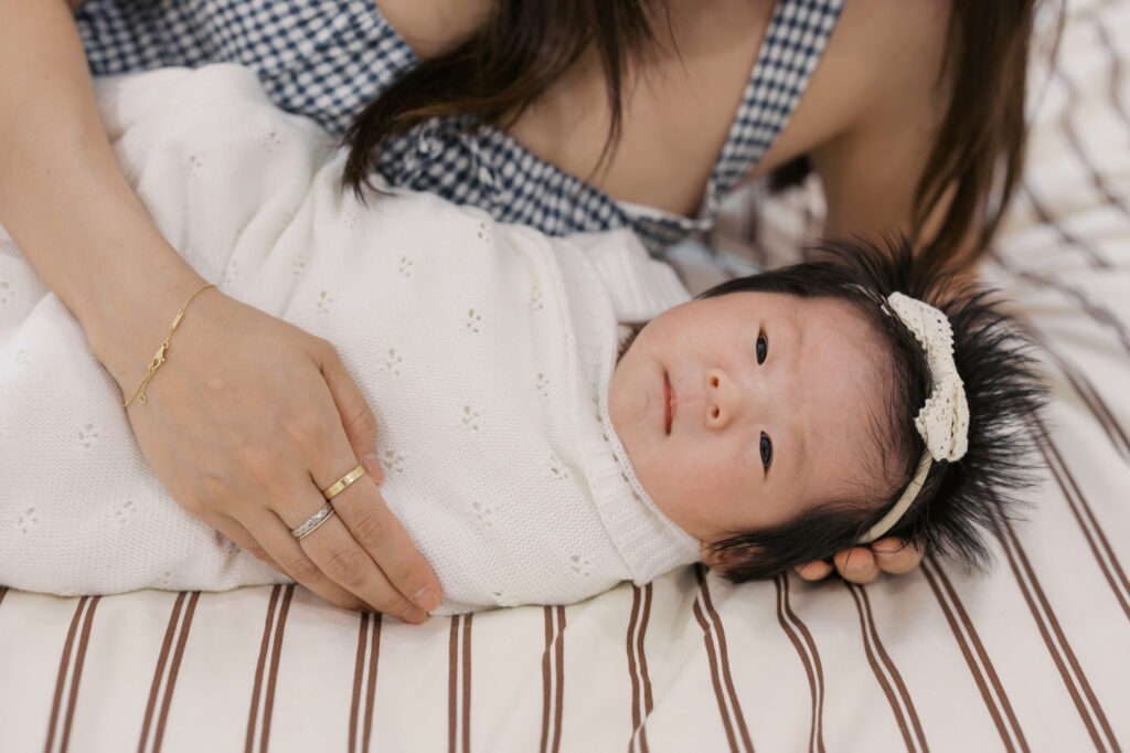 newborn baby girls wrapped in pointelle blanket lays on bed in moms arms looking at camera