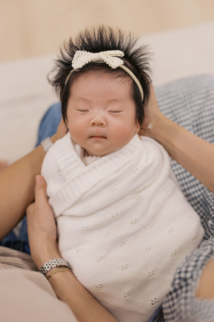 newborn baby girl at one month old in Santa Clara, wrapped in a white pointelle swaddle and held by her parents