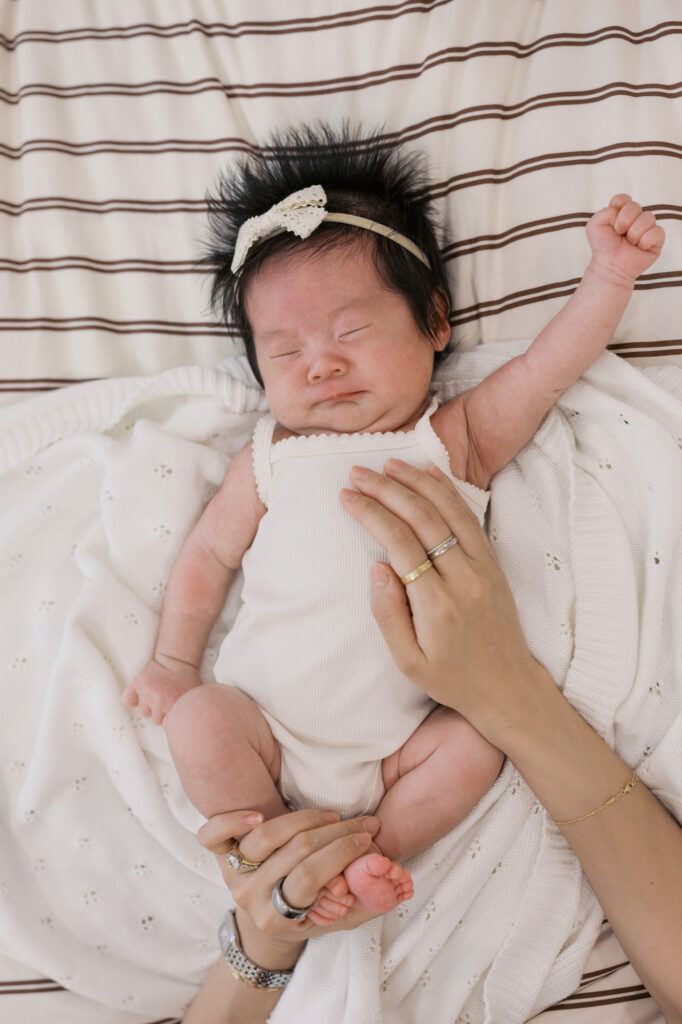 one month old baby girl stretches while laying on the bed during her Santa Clara newborn photography session