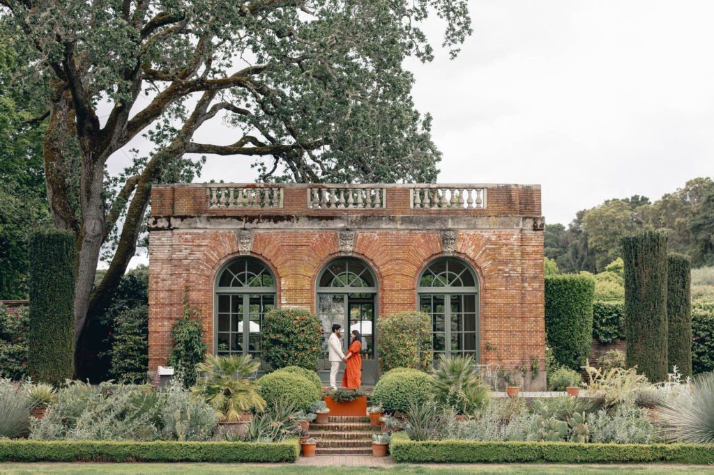 Expecting couple stand in front of Filoli's garden house during their Bay Area maternity photography session during the rose bloom