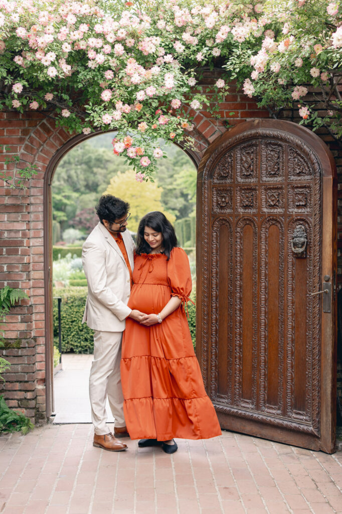 Filoli maternity session: expecting couple stand in front of Filoli's main archway under the climbing roses